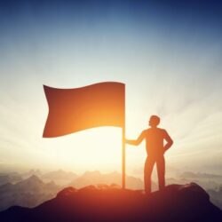 Proud man raising a flag on the peak of the mountain. Challenge, achievement